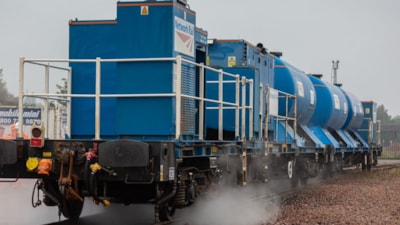 A railhead treatment train spraying water on track lined with autumn trees